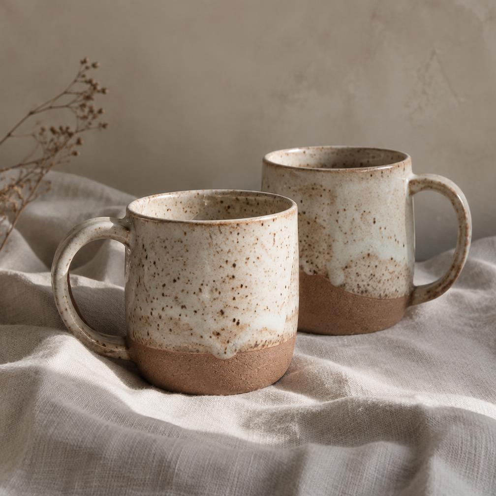 Two handmade ceramic mugs with speckled cream glaze